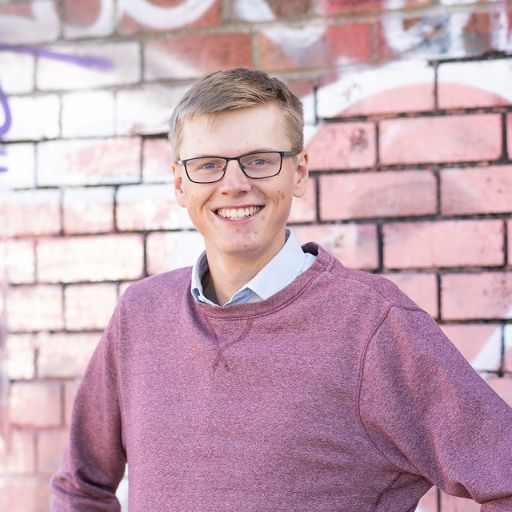 Jamie looking at the camera in front of a brick wall with street art