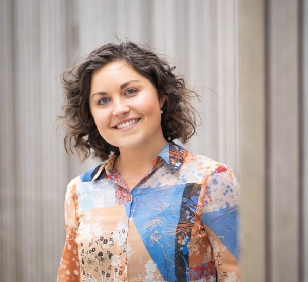 Woman in colourful blouse with short brown hair smiles at camera