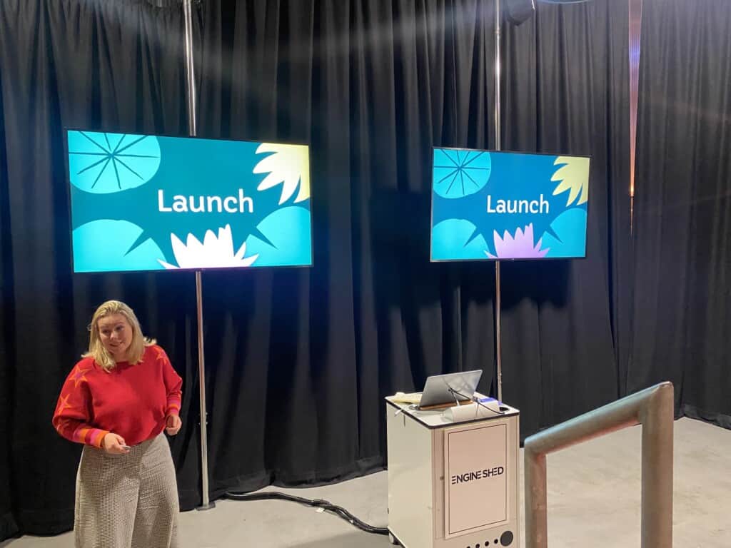 Woman talks in front of screens during presentation at event about how to sell more without costing the earth