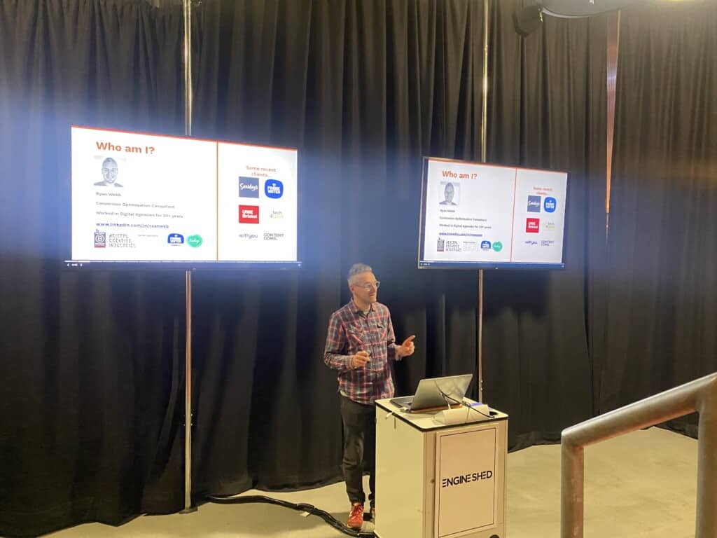 Man talks in front of screens during presentation at event about how to sell more without costing the earth