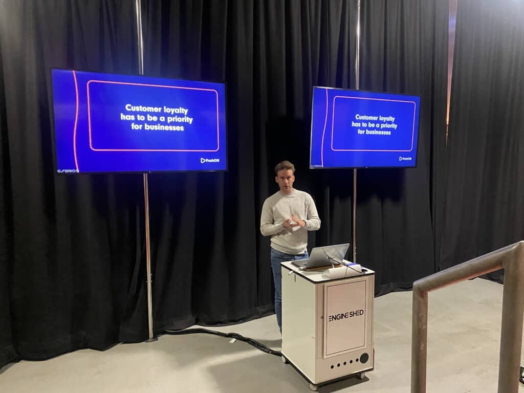 Man talks in front of screens during presentation at event about how to sell more without costing the earth