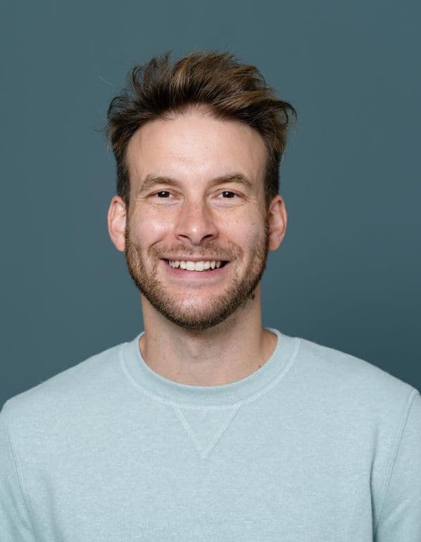 Man smiles in blue jumper against darker blue backdrop