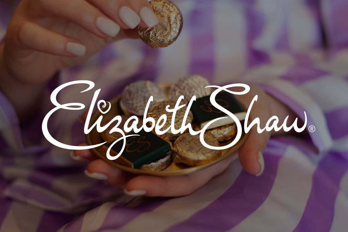 Screenshot of Elizabeth Shaw logo in front of image of woman's hands with chocolate