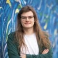 Mikey standing with arms folded and looking at the camera in front of street art