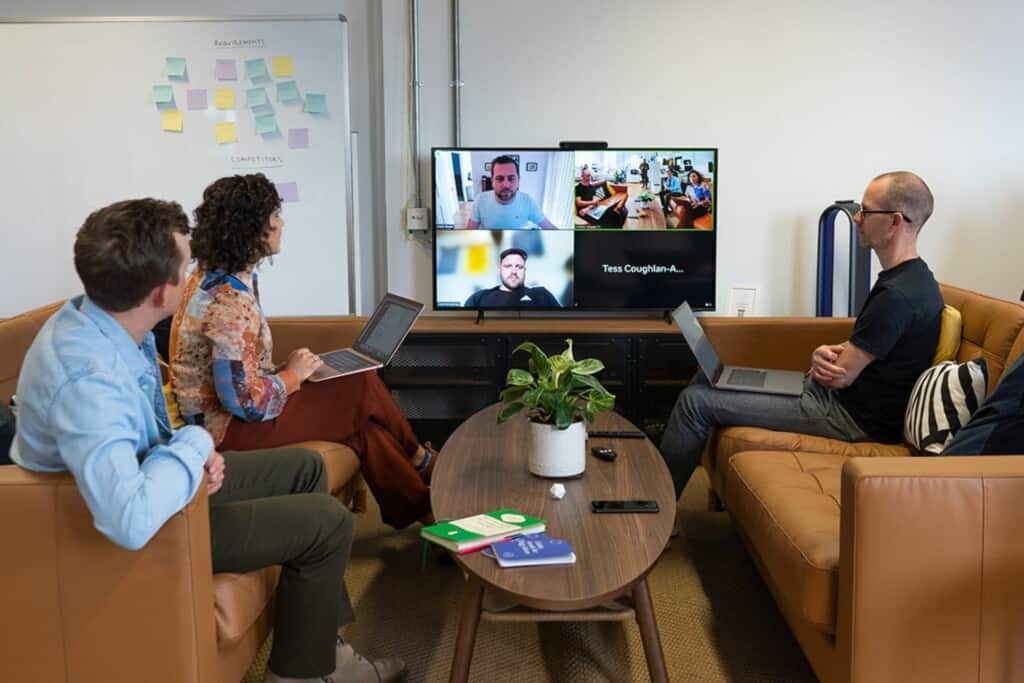 Hybrid meeting with three members of Atomic Smash's Sustainability Working Group sat on sofas in the office and another three members of the group dialling in remotely