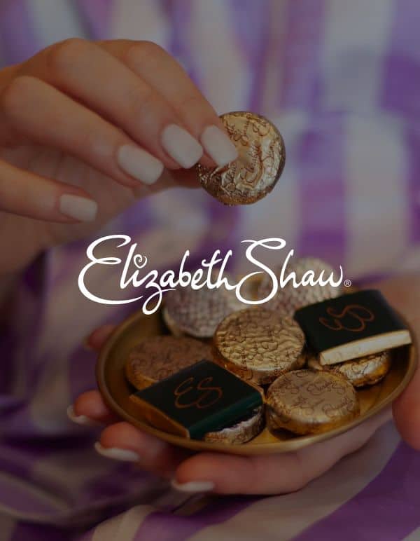 Screenshot of Elizabeth Shaw logo in front of image of woman's hands with chocolate