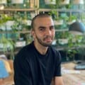Mohd wearing a black top in Atomic Smash's office space sat in front of a wall of plants