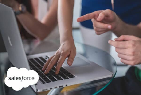 Close up shot showing team members around laptop, one pointing at the screen and another with fingertips on the keyboard, plus the salesforce logo