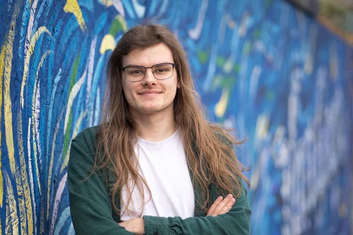 Mikey stood with arms crossed facing the camera, in front of a painted exterior